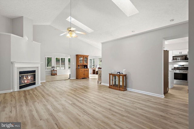 unfurnished living room with a skylight, light wood-type flooring, a textured ceiling, a tiled fireplace, and a ceiling fan