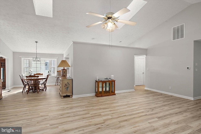 living room with light wood finished floors, ceiling fan, baseboards, a chandelier, and a textured ceiling