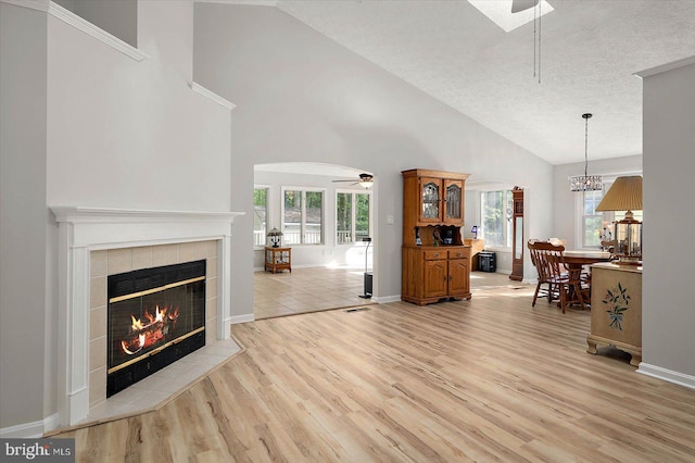 living room featuring a fireplace, ceiling fan, light wood-style flooring, high vaulted ceiling, and a textured ceiling