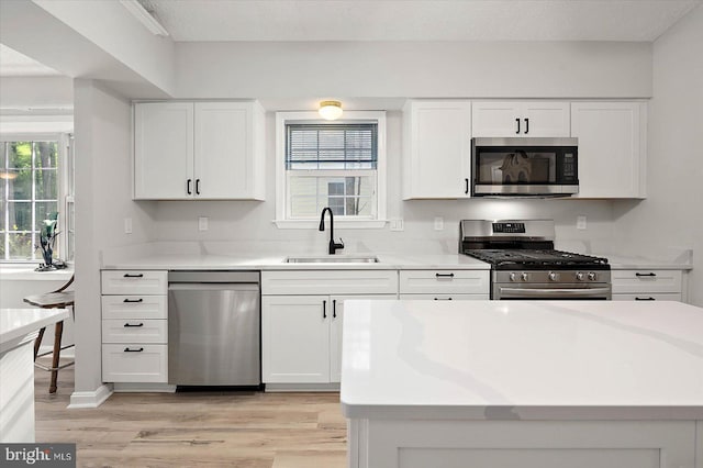 kitchen with appliances with stainless steel finishes, a sink, light wood finished floors, white cabinetry, and light countertops