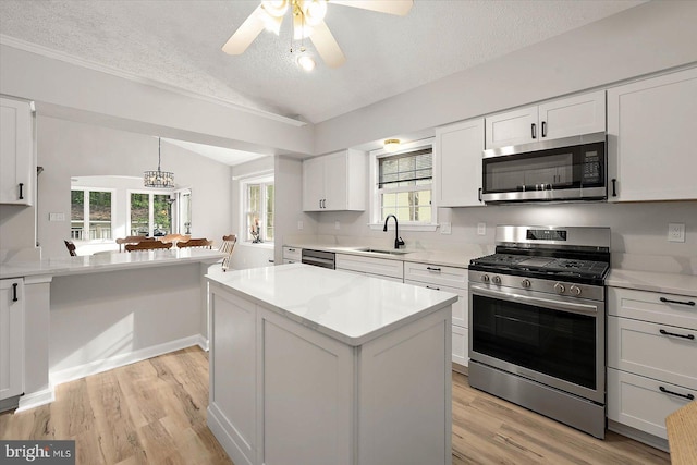 kitchen featuring appliances with stainless steel finishes, vaulted ceiling, a textured ceiling, a sink, and light countertops