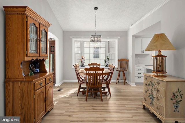 dining room featuring a textured ceiling, a chandelier, light wood-style flooring, and baseboards