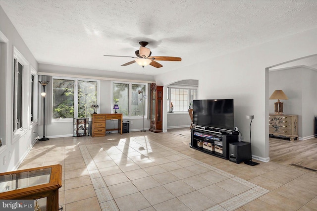 living room with light tile patterned floors, healthy amount of natural light, ceiling fan, a textured ceiling, and baseboards