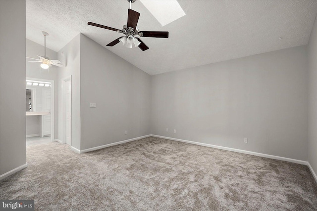 carpeted empty room featuring a ceiling fan, lofted ceiling, a textured ceiling, baseboards, and a skylight