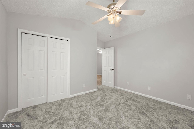 unfurnished bedroom featuring carpet floors, vaulted ceiling, baseboards, a closet, and a textured ceiling