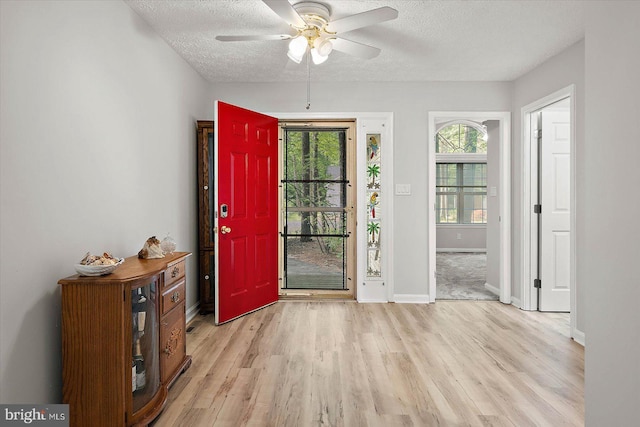 foyer with a textured ceiling, light wood-type flooring, a ceiling fan, and baseboards