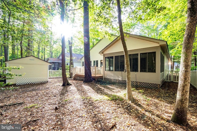 view of side of property featuring a sunroom, a deck, an outdoor structure, and fence