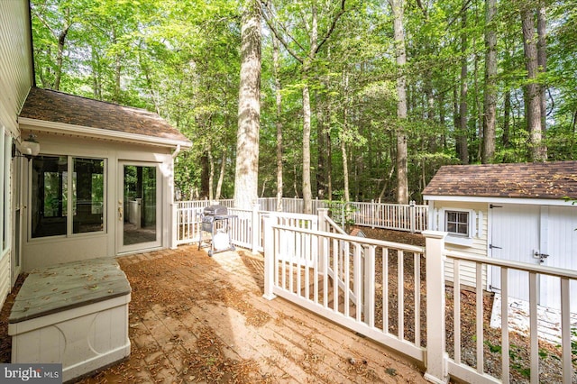 wooden deck with a grill, fence, a storage unit, and an outbuilding