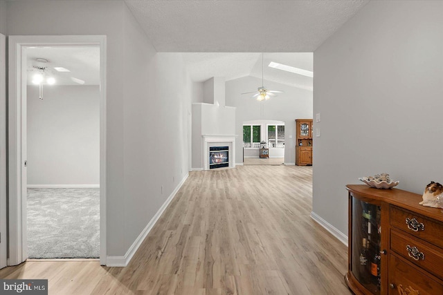 hallway featuring light wood finished floors, baseboards, and vaulted ceiling