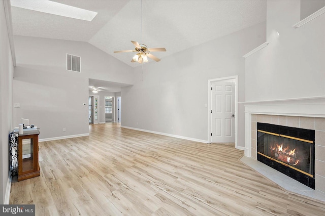 unfurnished living room with a ceiling fan, wood finished floors, a skylight, a tiled fireplace, and high vaulted ceiling