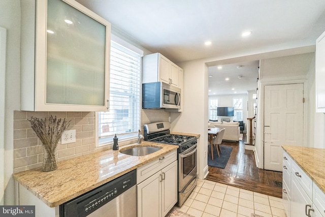kitchen featuring light stone counters, light tile patterned floors, backsplash, stainless steel appliances, and a sink