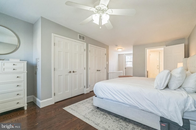bedroom featuring dark wood finished floors, connected bathroom, visible vents, multiple closets, and baseboards