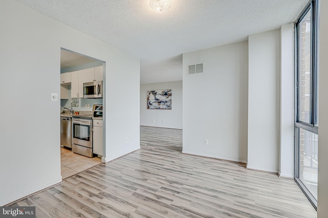 2311 Pimmit Dr Unit 1102, Falls Church, VA 22043 - kitchen featuring stainless steel appliances, light wood-style floors, a textured ceiling, white cabinets, and light countertops