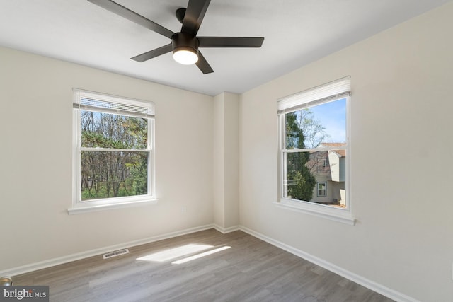 spare room featuring visible vents, baseboards, plenty of natural light, and wood finished floors