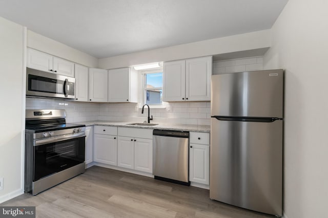 kitchen featuring light wood-style flooring, white cabinets, a sink, stainless steel appliances, and decorative backsplash
