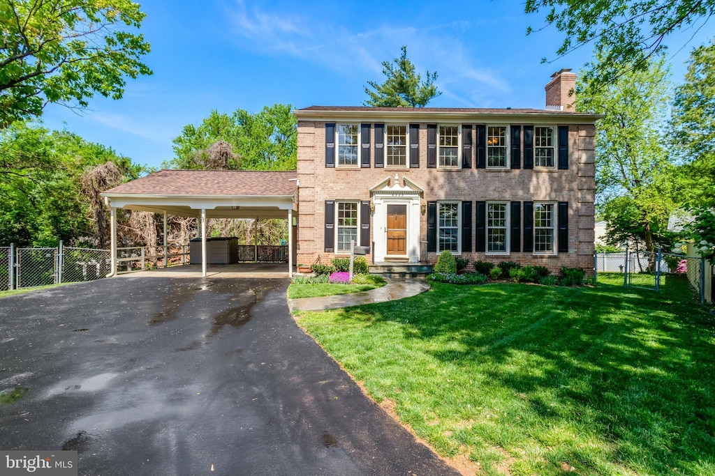 colonial inspired home with fence, a front lawn, brick siding, a chimney, and driveway