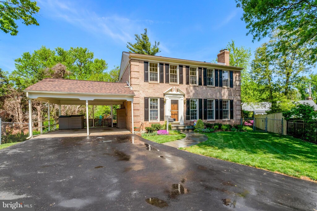colonial-style house with fence, a front yard, a chimney, brick siding, and driveway