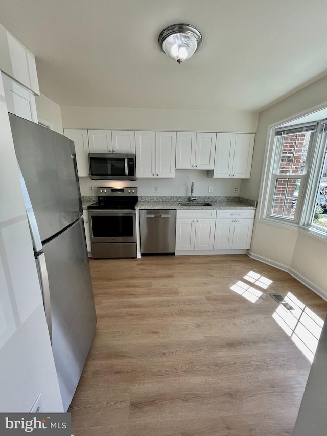 kitchen featuring white cabinets, light stone counters, a sink, light wood-style flooring, and appliances with stainless steel finishes