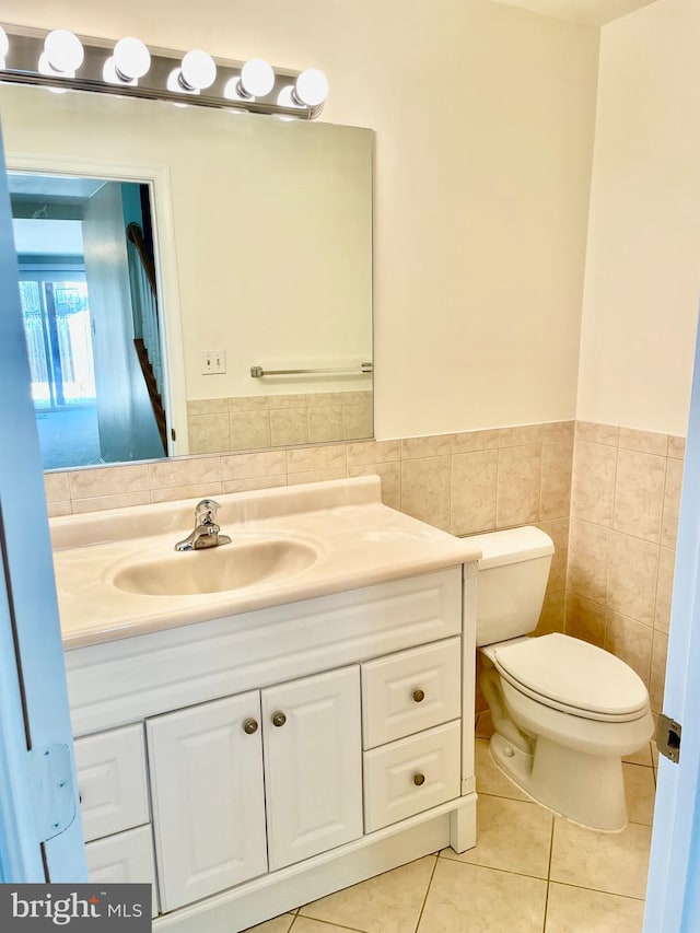 half bath with tile patterned floors, vanity, toilet, and tile walls