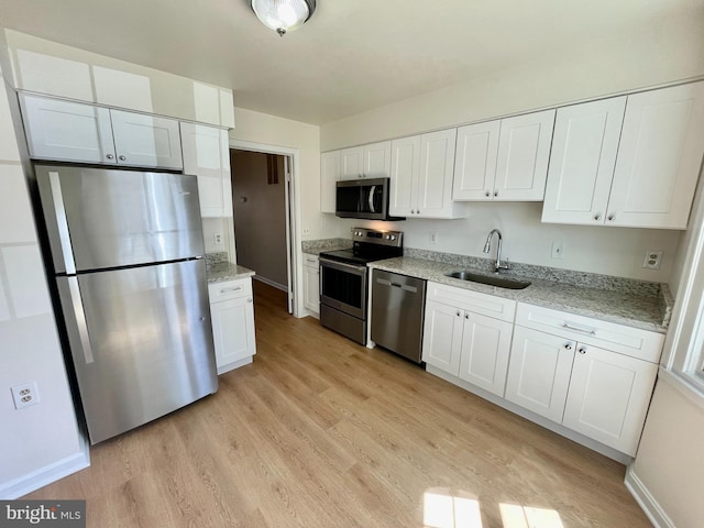 kitchen with a sink, appliances with stainless steel finishes, light wood-style flooring, and white cabinetry