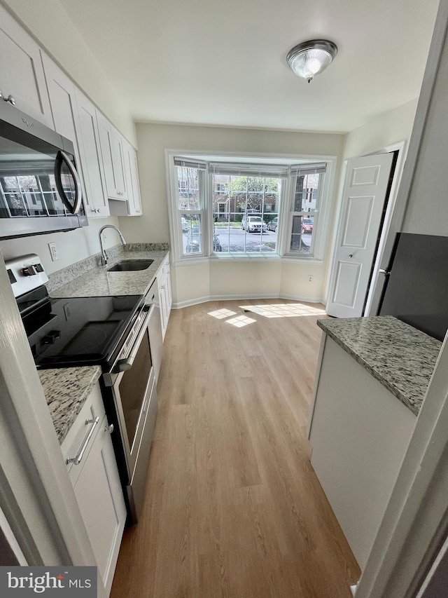 kitchen with a sink, light stone counters, white cabinets, light wood finished floors, and stainless steel appliances
