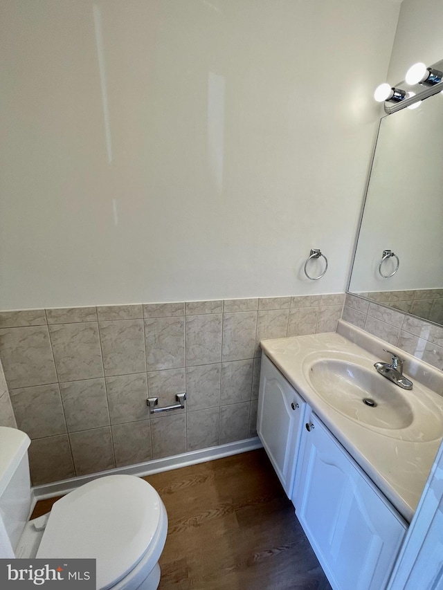bathroom with toilet, tile walls, wood finished floors, and vanity