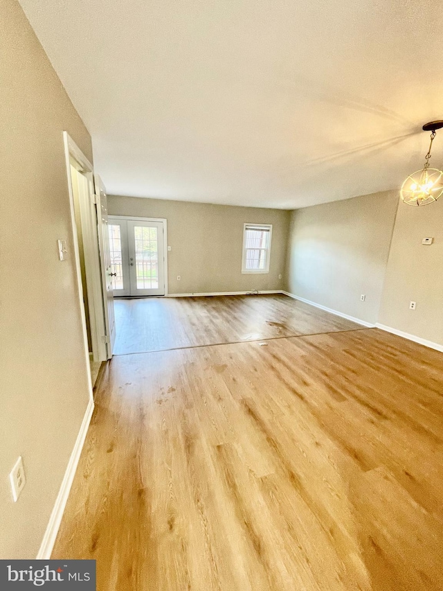 spare room with an inviting chandelier, baseboards, french doors, and wood finished floors