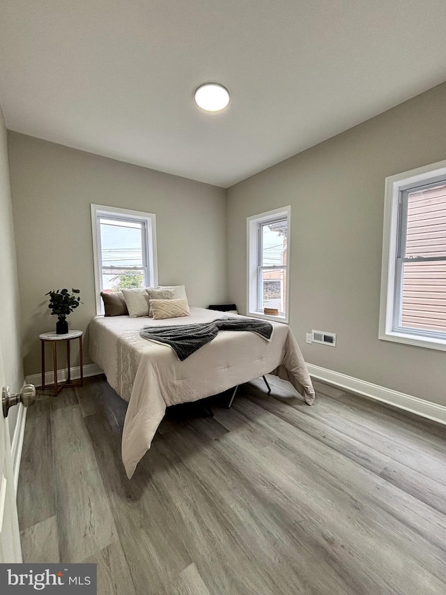 bedroom with wood finished floors, baseboards, multiple windows, and visible vents