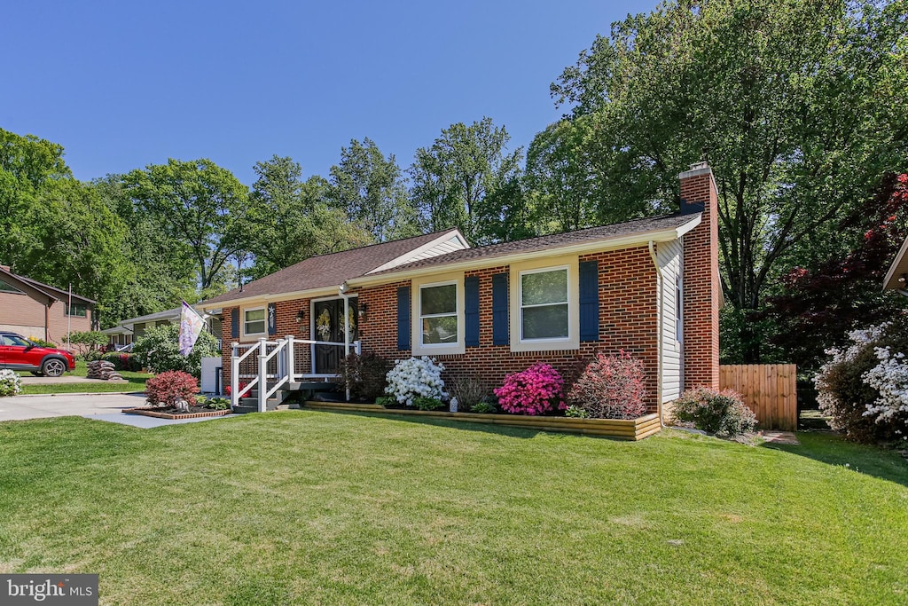 single story home featuring brick siding, a front lawn, fence, and a chimney