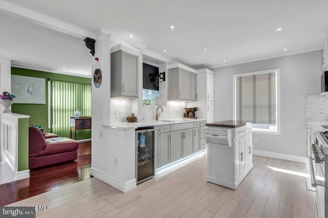 kitchen featuring light wood-style flooring, beverage cooler, ornamental molding, and backsplash