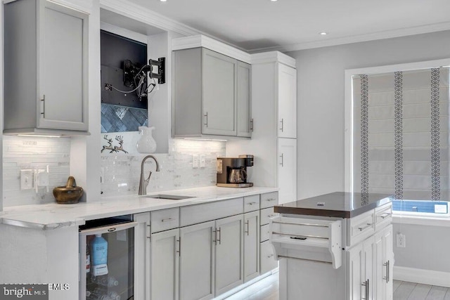 kitchen with a sink, backsplash, ornamental molding, and light stone counters
