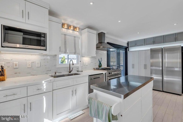 kitchen with appliances with stainless steel finishes, a sink, wall chimney exhaust hood, and backsplash
