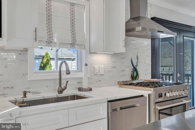 kitchen featuring tasteful backsplash, wall chimney range hood, white cabinetry, stainless steel appliances, and a sink