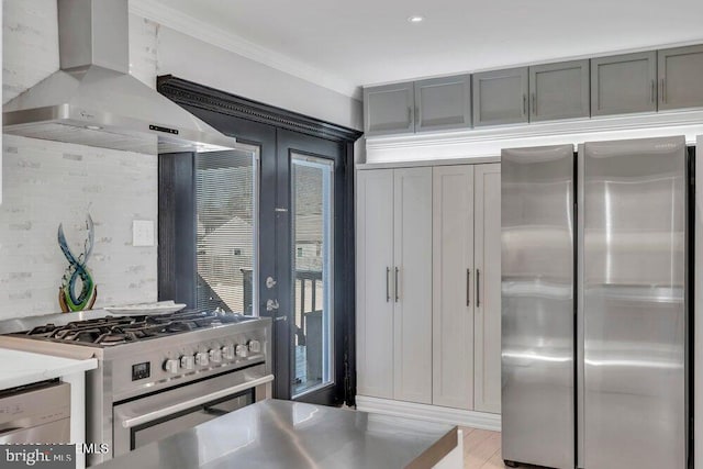 kitchen with tasteful backsplash, wall chimney range hood, appliances with stainless steel finishes, light countertops, and gray cabinetry