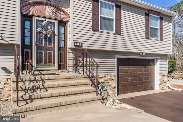 entrance to property featuring driveway, a garage, and stone siding