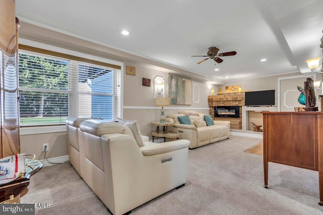 living room featuring a glass covered fireplace, light colored carpet, crown molding, and a ceiling fan