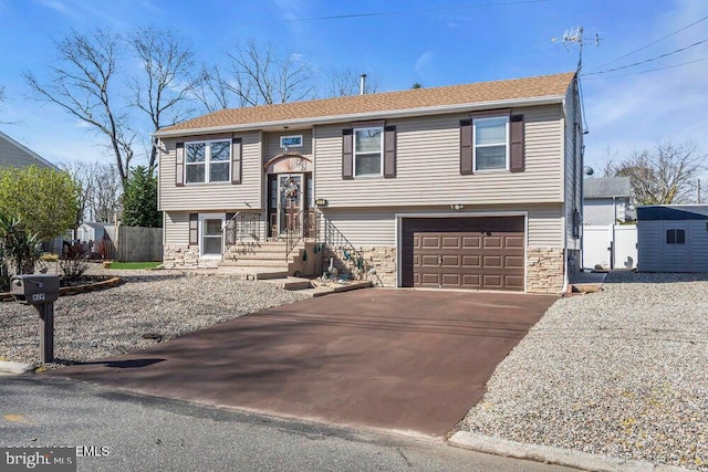 split foyer home featuring an outdoor structure, driveway, stone siding, an attached garage, and fence