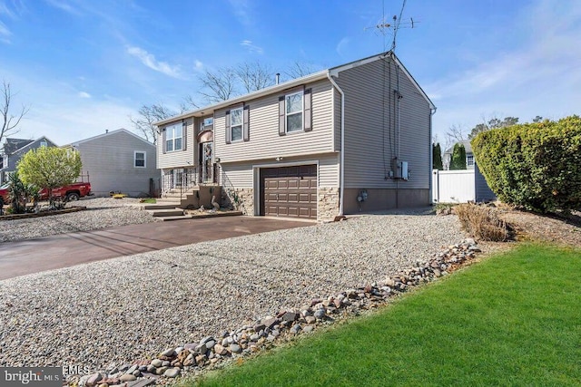 bi-level home featuring an attached garage, driveway, and fence