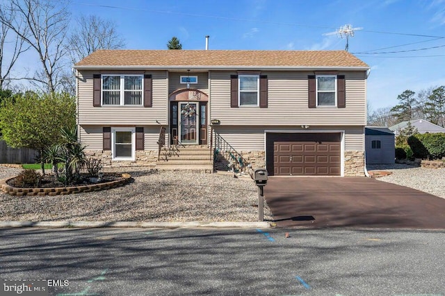 raised ranch featuring aphalt driveway, stone siding, and an attached garage