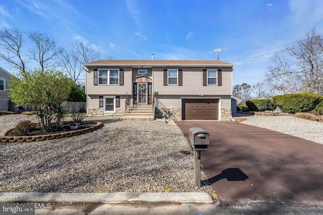 raised ranch featuring an attached garage, stone siding, and driveway