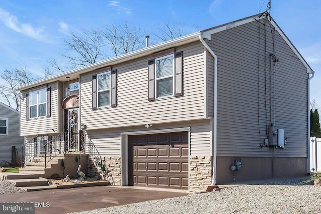 bi-level home with concrete driveway, stone siding, and an attached garage