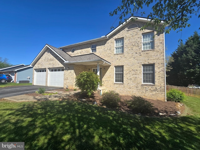 traditional-style house featuring fence, an attached garage, brick siding, aphalt driveway, and a front yard