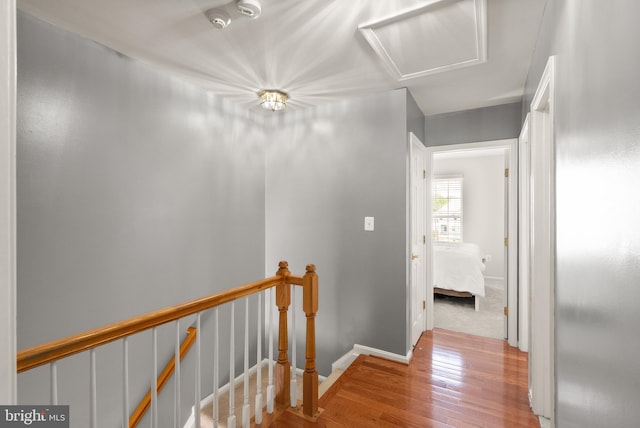 corridor featuring baseboards, wood finished floors, and an upstairs landing