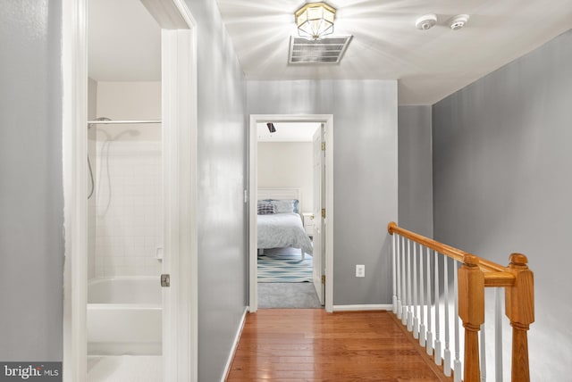 hall featuring hardwood / wood-style flooring, an upstairs landing, and visible vents