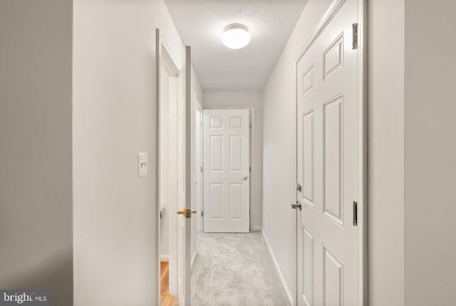 hallway with baseboards, a textured ceiling, and light carpet