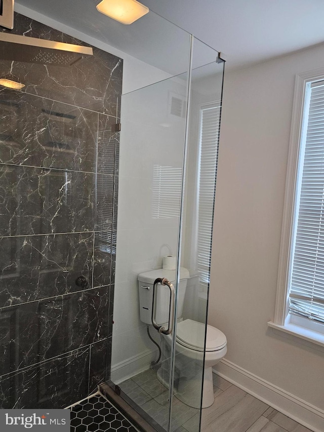 bathroom featuring visible vents, toilet, wood finished floors, a stall shower, and baseboards