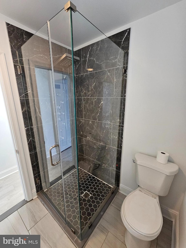 bathroom featuring toilet, a stall shower, and baseboards
