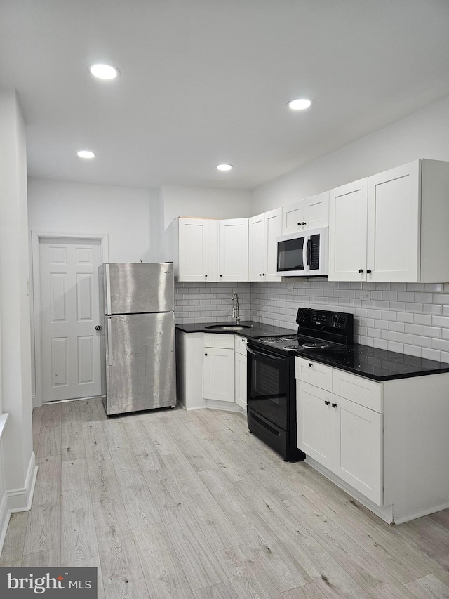 kitchen featuring a sink, freestanding refrigerator, black / electric stove, backsplash, and light wood-style flooring