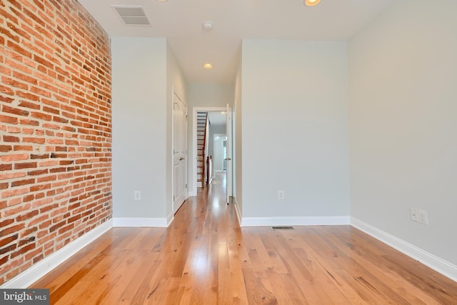 unfurnished room with brick wall, light wood-style floors, visible vents, and baseboards