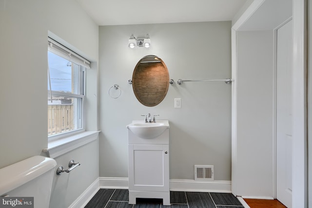 half bath with vanity, visible vents, baseboards, and toilet